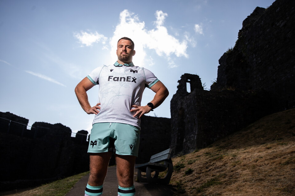 Morgan Morris stands in front of Oystermouth Castle, wearing Ospreys 2627 away jersey