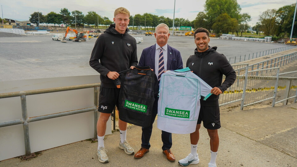 Ospreys' Lewis Edwards and Keelan Giles stand with Swansea Building Society holding the sponsored home and away jerseys as St Helen's stadium is redeveloped in the background